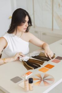 A woman reviewing hair color samples with cosmetics and swatches on a salon table.